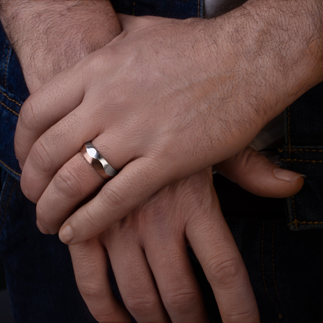 Man's hand with modern silver wedding ring on denim.