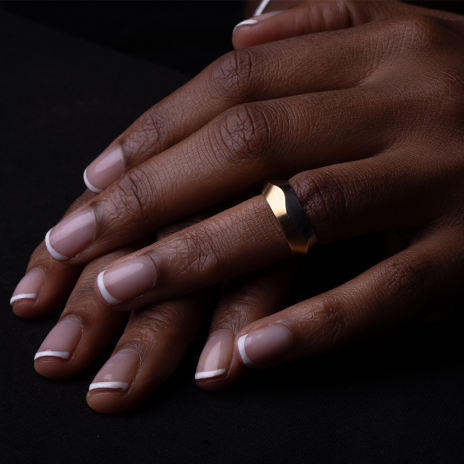 Elegant hands with matte gold wedding band on black.