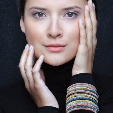Woman with subtle makeup touching face wearing bangles and turtleneck.