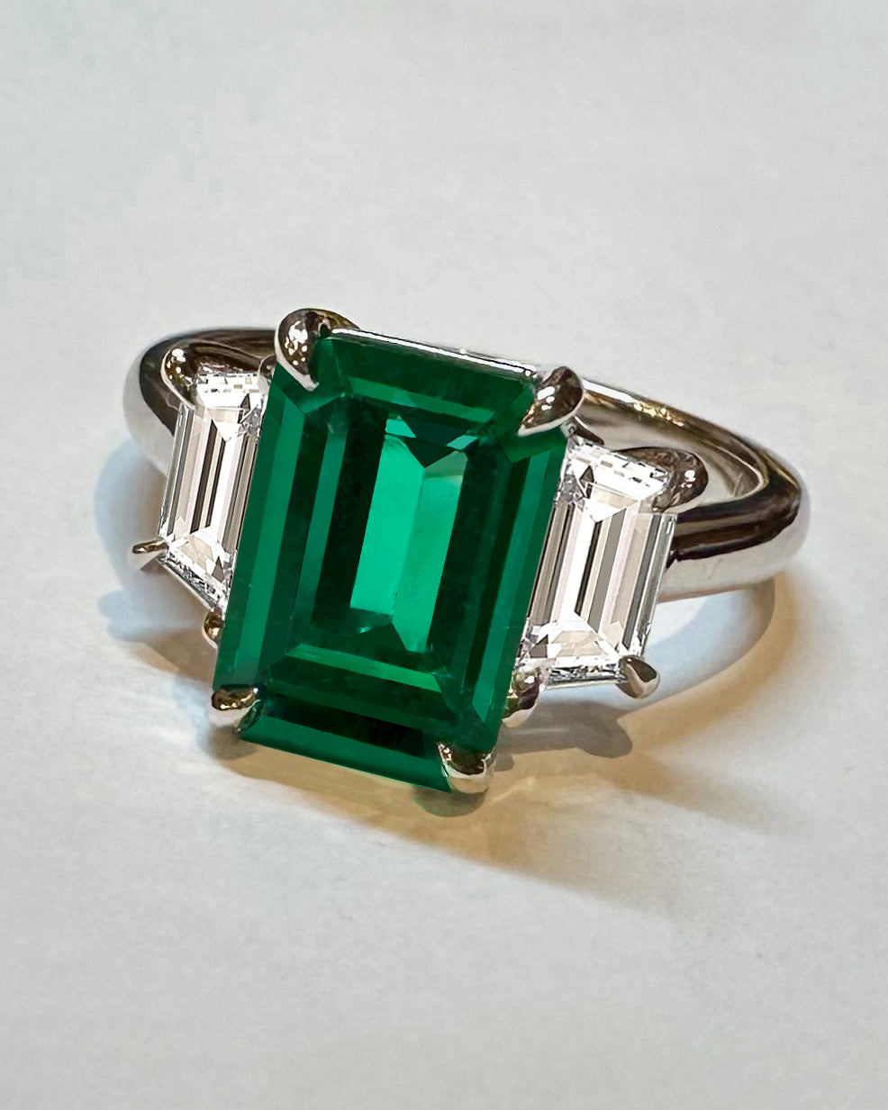 Emerald ring with diamond baguettes on white background.