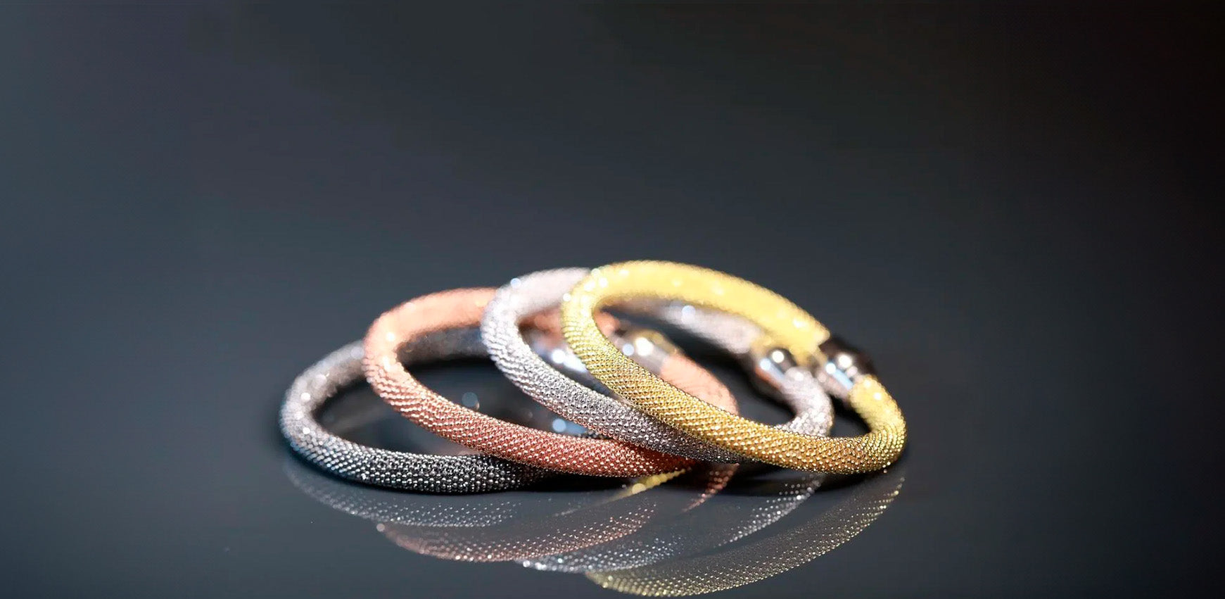 Four sparkling intertwined bangle bracelets on dark surface.