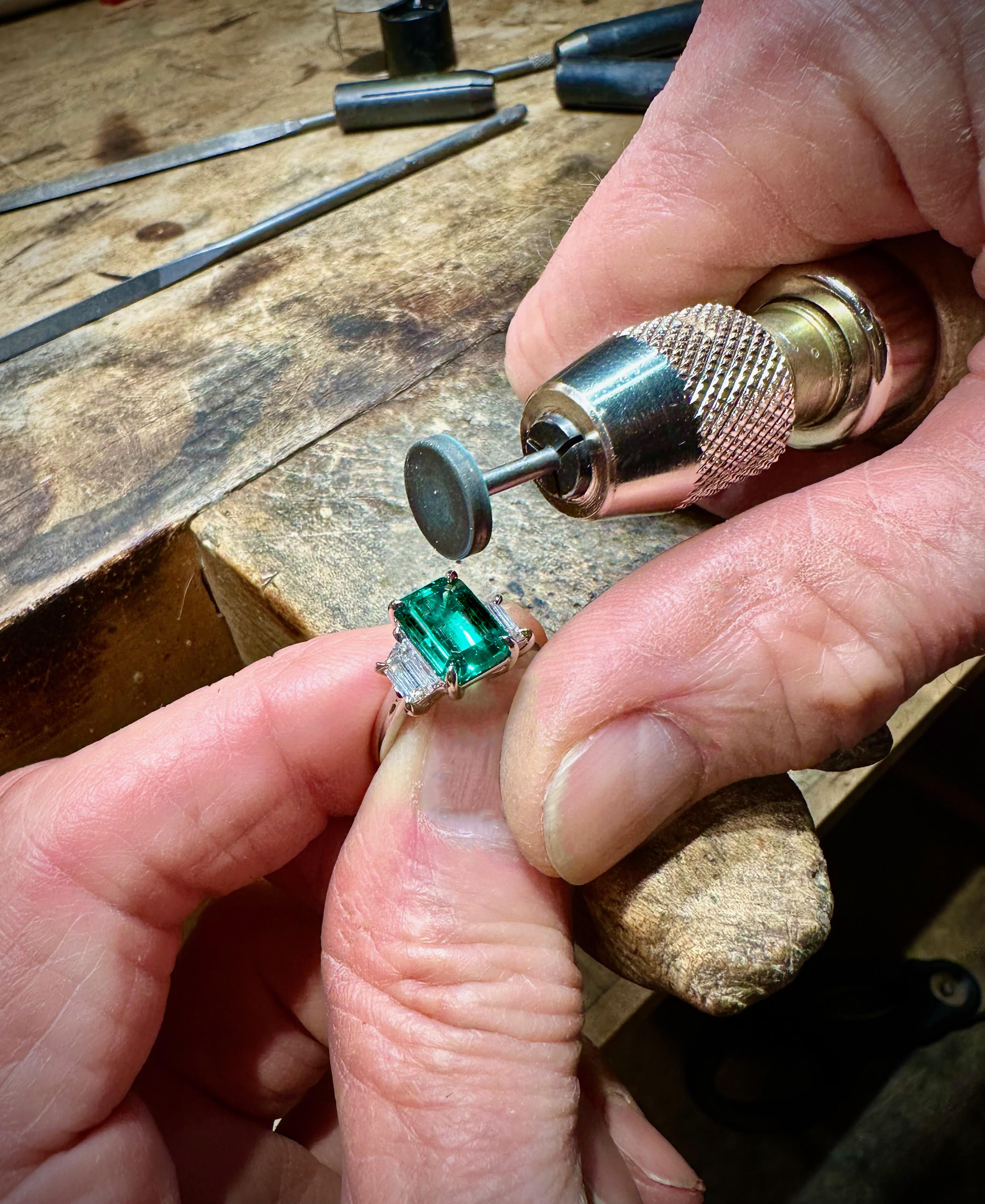 Jeweler polishing emerald ring at workbench.